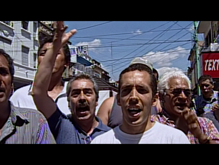 Grainy still of video footage of a group of men in t-shirts and polos marching down the streets, their arms up in the air