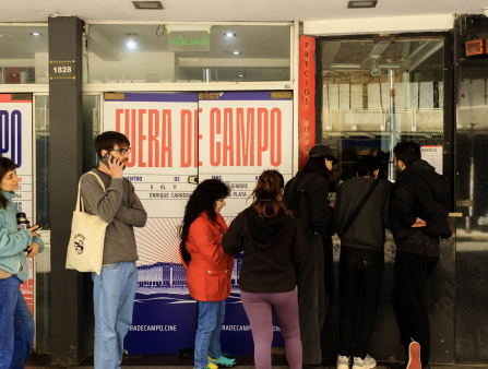 A young crowd gathers in a line outside of a venue that has a giant sign that reads Fuera de Campo