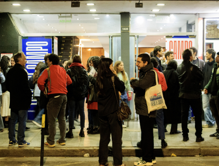 Crowds in warm clothing and tote bags gather around outside a movie theater venue