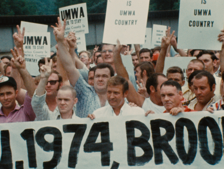 A crowd of white men holding signs promoting "UMWA" and raising arms