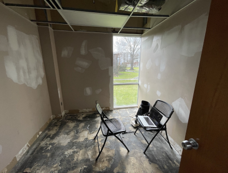 Empty room with two black foldout chairs, one of which has an open laptop on them