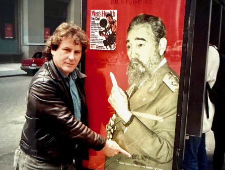 A man in a leather jacket points at an ad on a bus stop of another man pointing up