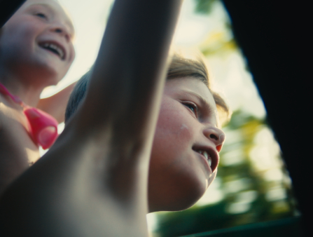 A young boy and girl smile and appear to face strong wind, shot from a low angle