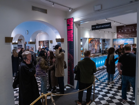 People gather in a white lobby space with checkered black and white tile flooring. A banner on the wall reads CPH:DOX
