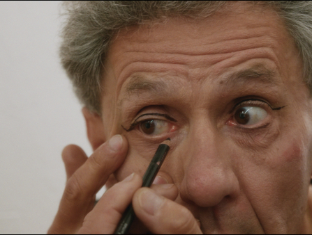 Close up of a wrinkled, greying face applying eyeliner