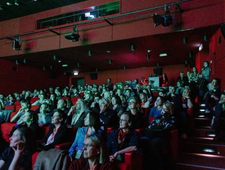 A red theater filled with people wearing orange lanyards illuminated by green light