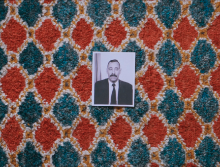A black and white portrait of a man in a suit rests on a textile patterned with blue and orange diamonds