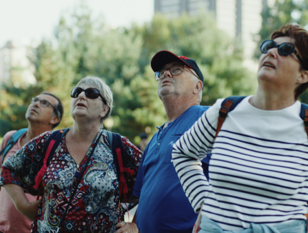A row of four older white people, two men in glasses and two women in sunglasses, look directly up
