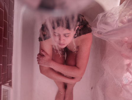A woman sits in a bathtub with pink curtains. Shot from above