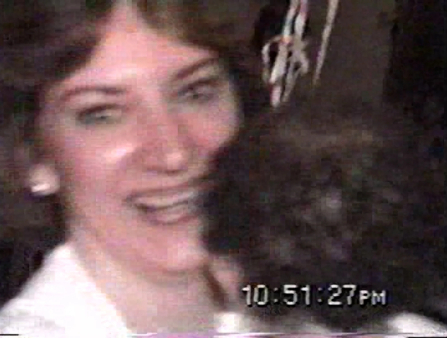 Low resolution close-up of a woman laughing, with another figure's head of black, curly hair partially obscuring her. A timestamp at the bottom right reads 10:51:27PM