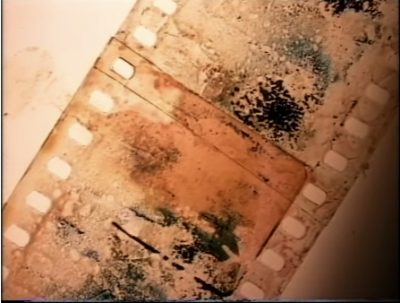 A strip of orange celluloid with black imprints runs diagonal to the frame
