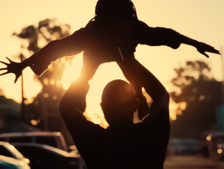 A man is lifting up a child against sunset