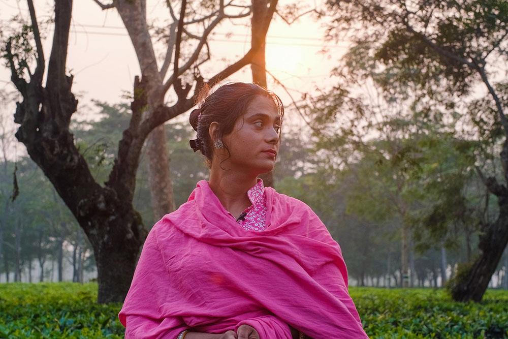 An woman wearing pink stands in nature, the sun setting behind her