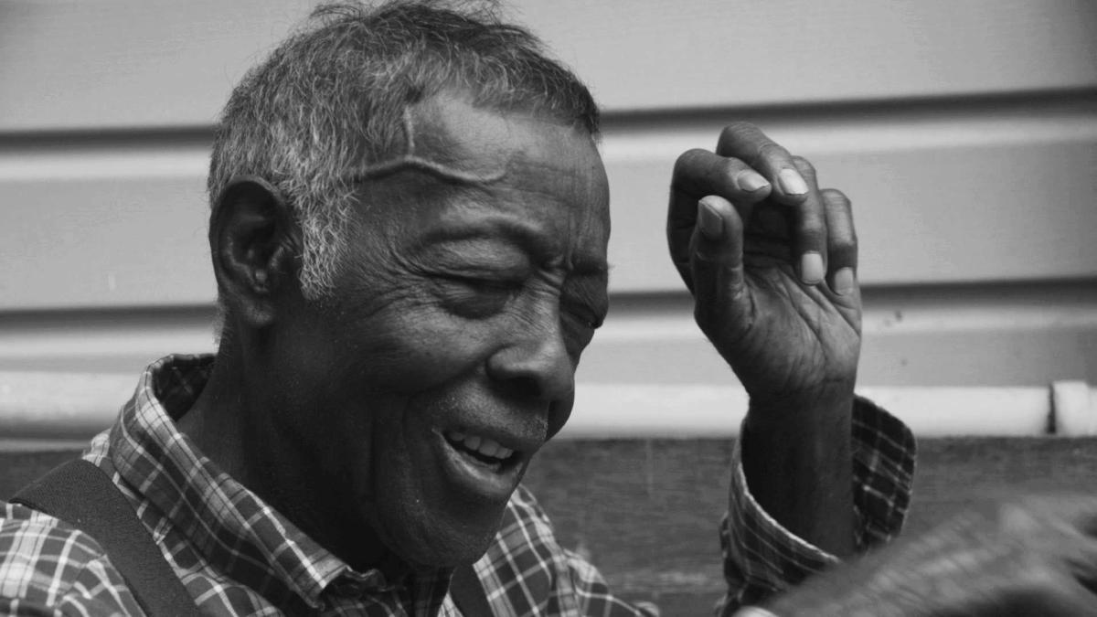 A black & white image of an elderly man of African-American descent sitting on a porch.