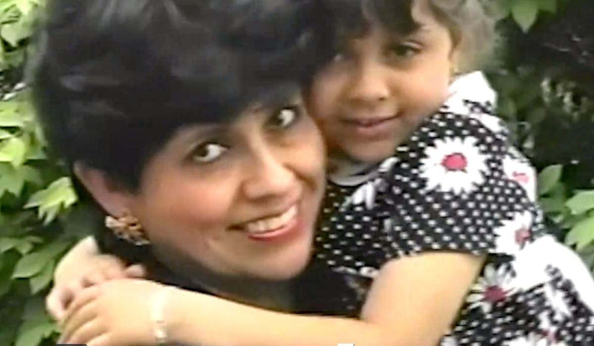 A mom and her daughter embrace in a close up of their faces, the little girl wearing a black and white polka dot dress. 
