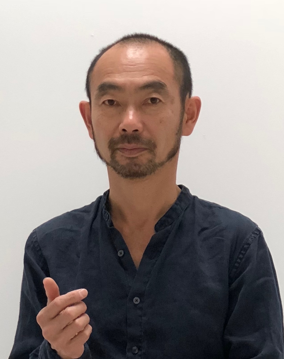 Headshot of a middle-aged male of Asian decent, wearing a black shirt, in front of a white wall.
