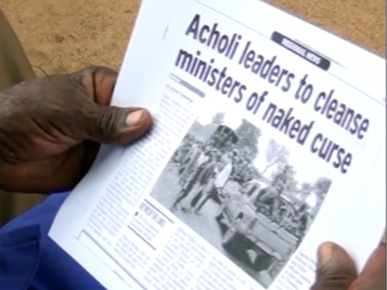 Image of two hands holding a folded newspaper with the headline "Acholi leaders to cleanse ministers of naked curse"