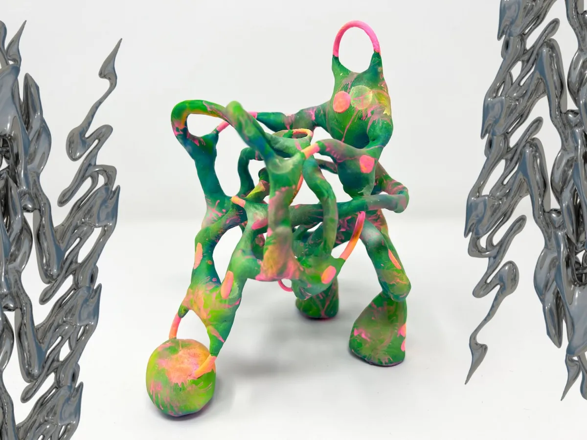 An art piece by Nat Decker: on the left and right edges of a green, pink, and orange twisted 3D sculpture that looks like it’s made of clay we see 3D iridescent dark grey chrome squiggles