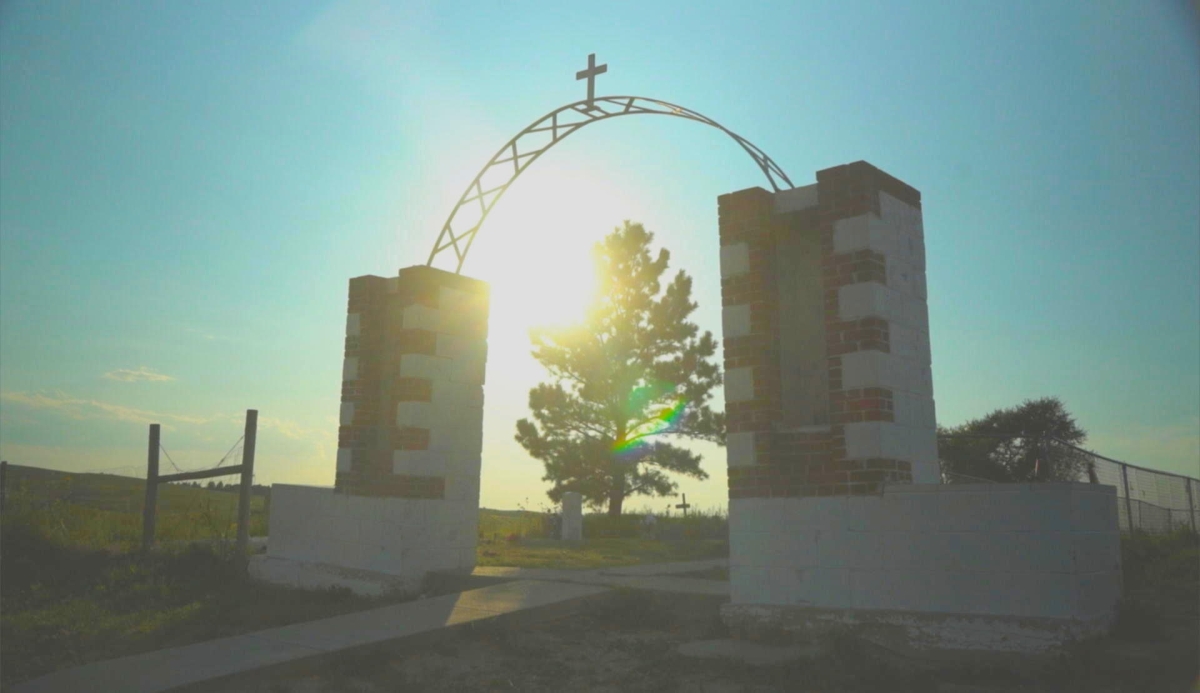 Wounded Knee Memorial arch framing a tree with a ray of sunlight