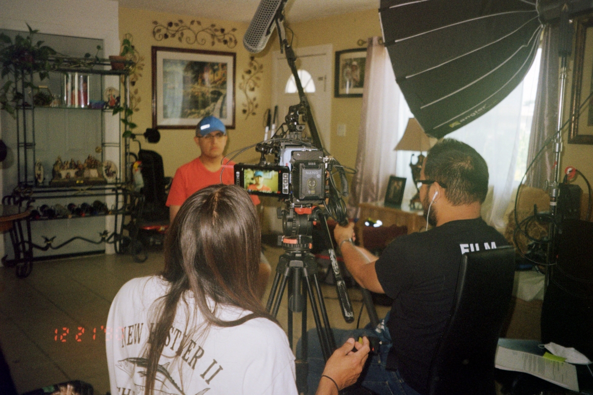 Behind-the-scenes photo inside a house. Pedro sits in front of the camera with Set holding a boom microphone next to cinematographer Richard Hama.