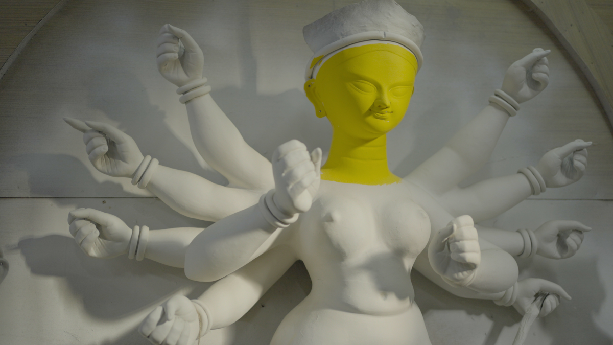 A white clay figure of a Hindu goddess with a face that is painted yellow.