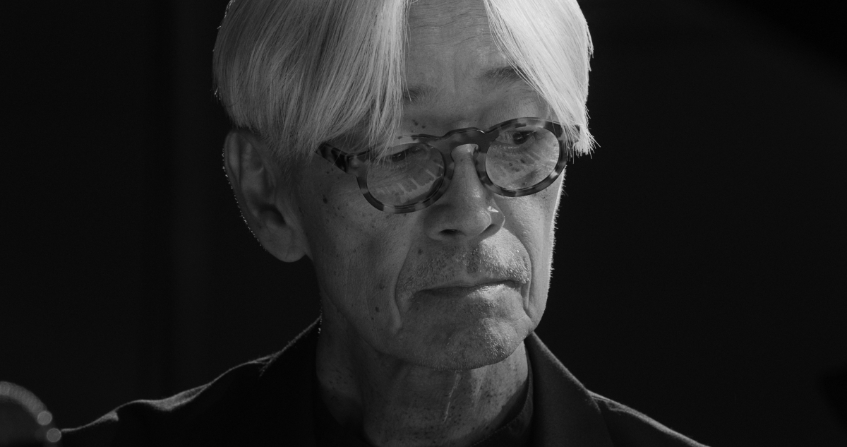 Still image from 'Ryuichi Sakamoto | Opus' depicting Sakamoto, an elderly Asian man wearing tortoiseshell glasses and with a fall of white hair over his forehead.