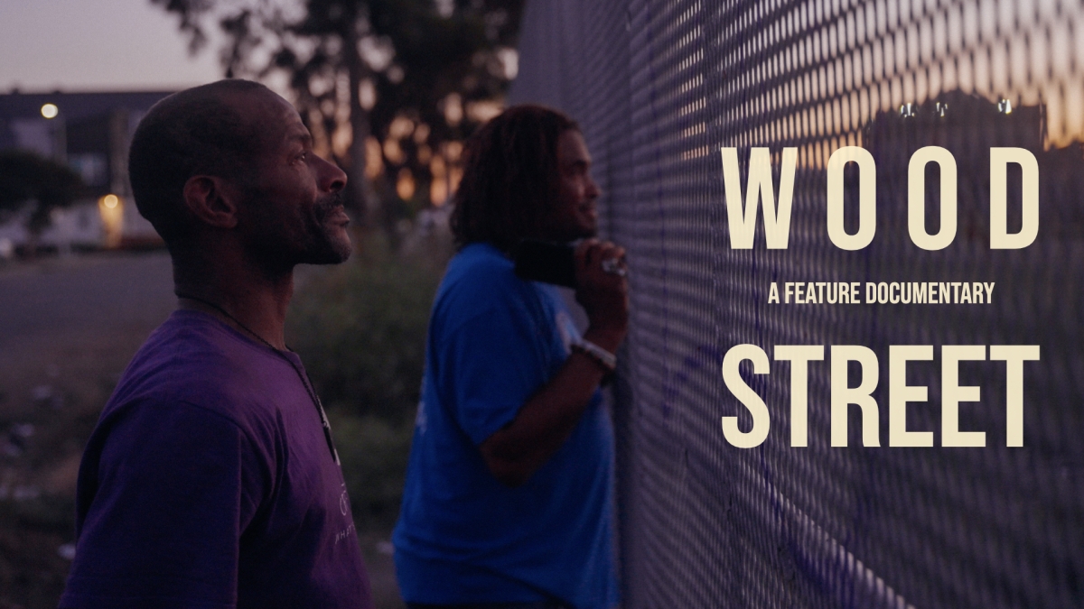 Two black men stand at a fence. Text on the right side of the image reads: Wood Street, a feature documentary.