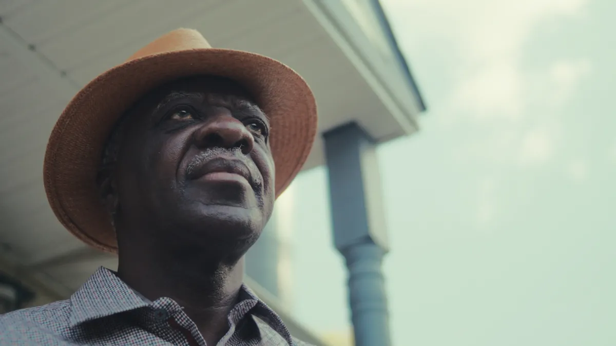 A Herero man wearing a straw hat looking beyond his front porch.