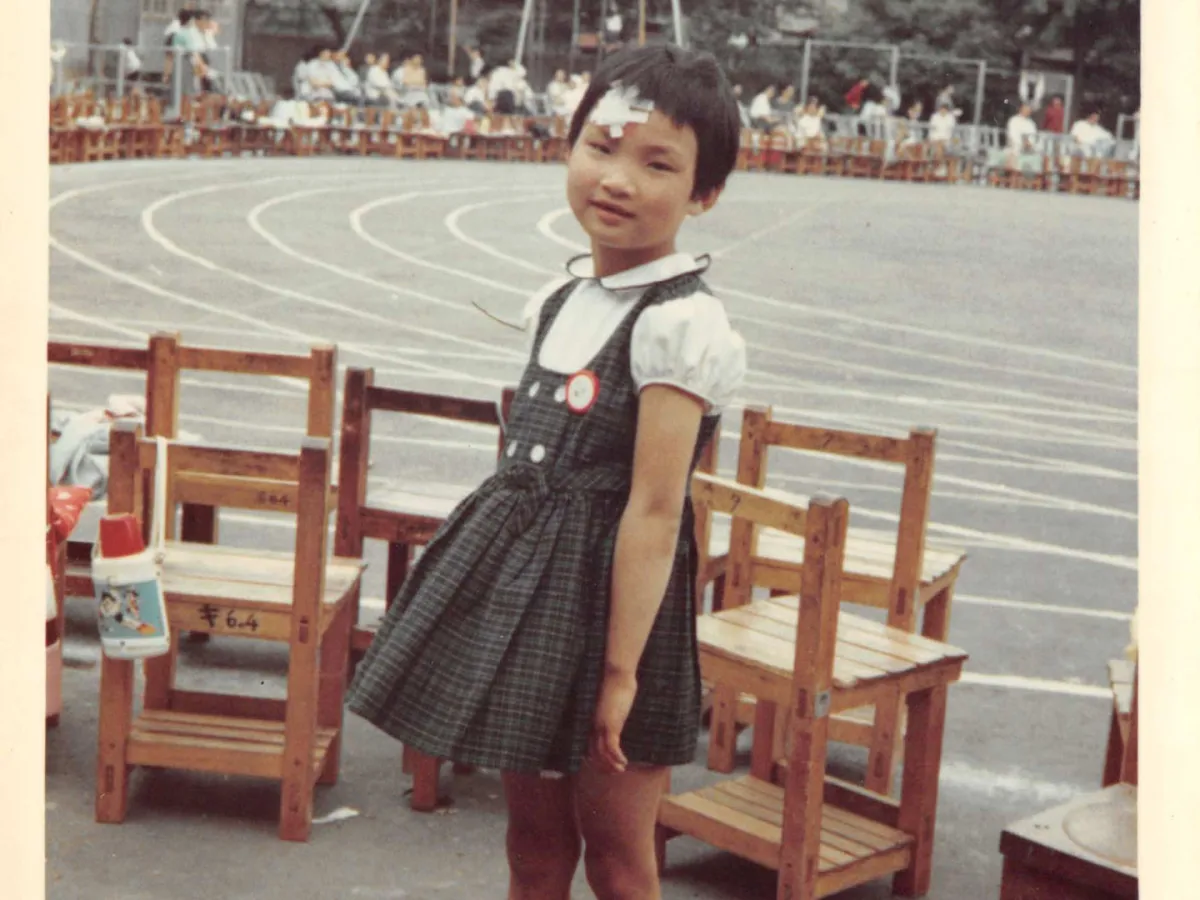 A young girl stands next to a race track, surrounded by empty wooden chairs.