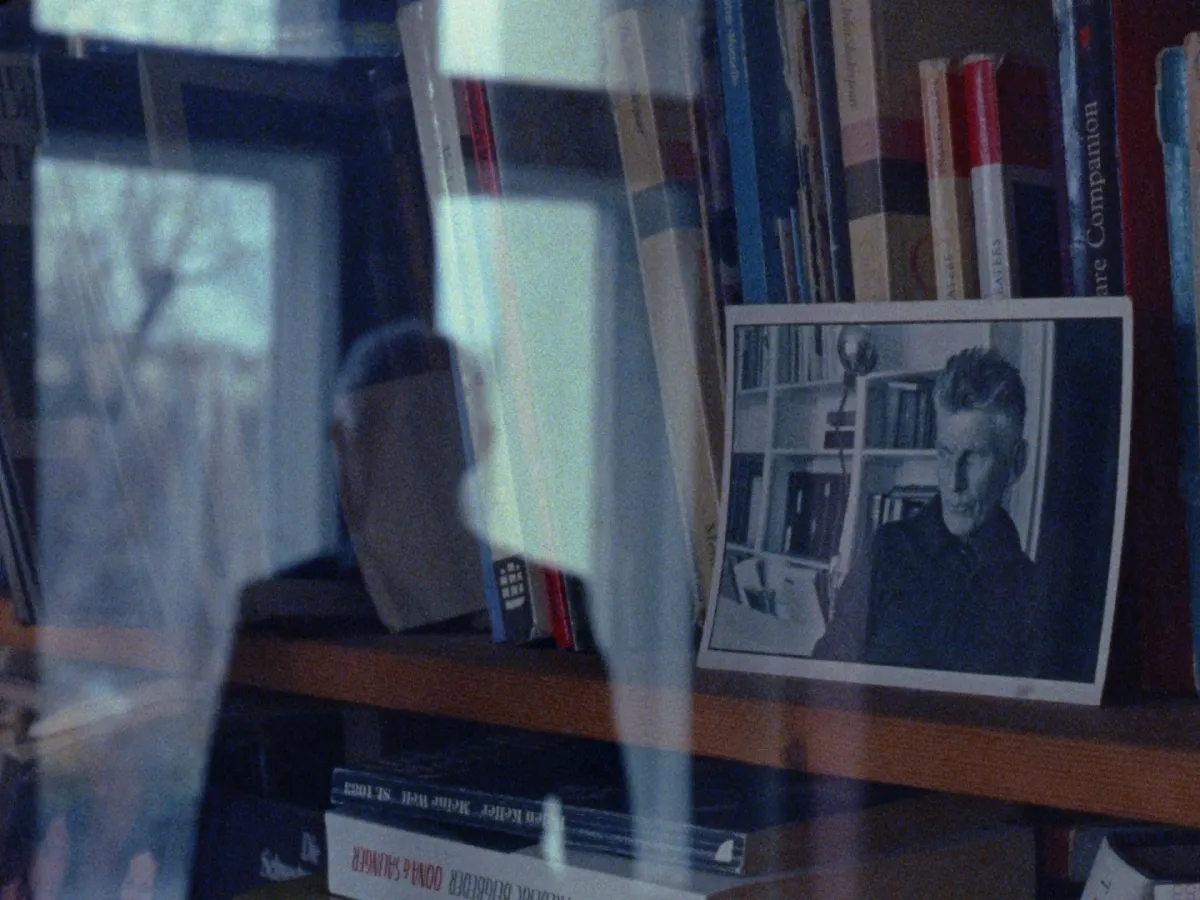 A man is reflected in the glass of a cabinet window. A photograph is visible through the glass panes.