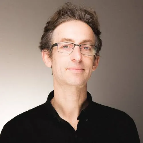 Headshot of a white man with thin-rimmed black glasses and a clean-shaven face.