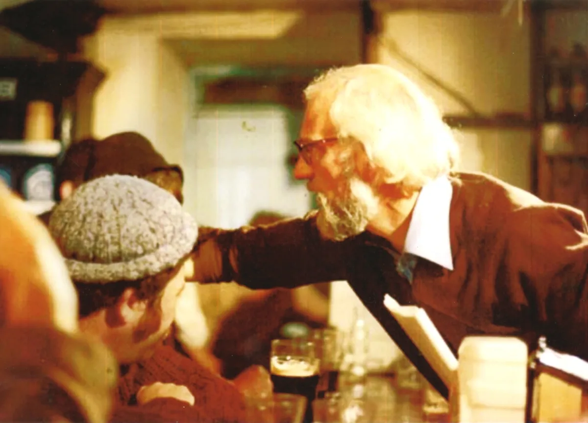 In a crowded bar, a man reaches over the bar.