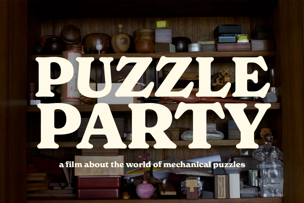 A wood cabinet with shelves full of mechanical puzzles. The puzzles are all manners of shapes and sizes, and crafted from a variety of materials. Text on the screen reads Puzzle Party, a film about the world of mechanical puzzles.