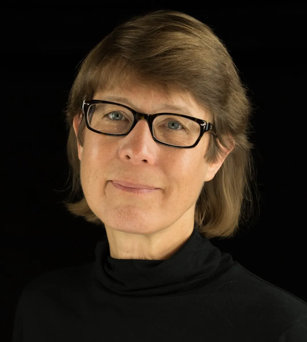 Headshot photo of Linda Tadic, a white woman with short brown hair, wearing black frame glasses and a black sweater.
