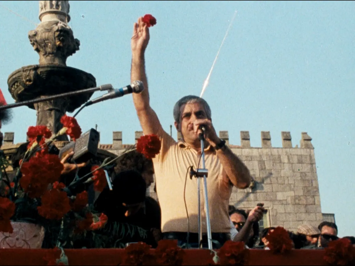 Grainy image of a man giving a public speech, while raising his right arm.