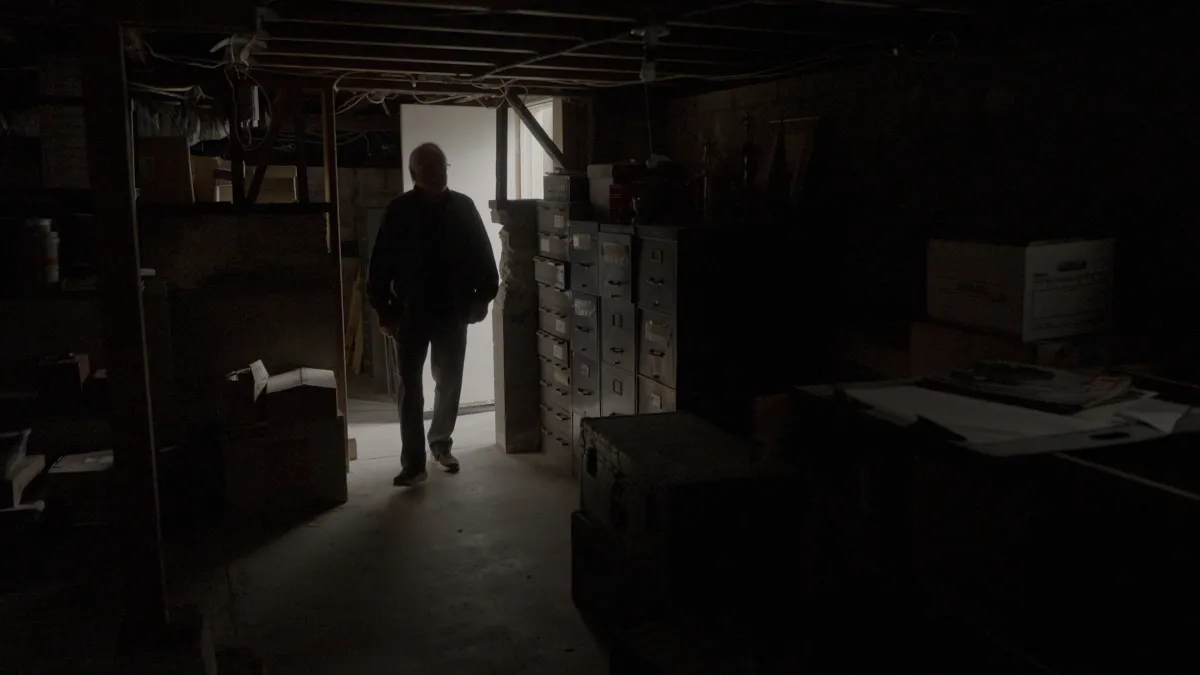 A man is silhouetted as he enters a basement filled with file cabinets and boxes.