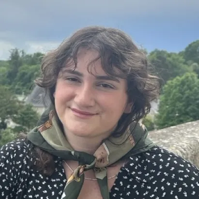 A young white woman with brown hair and a scarf tied around her neck smiles at the camera.