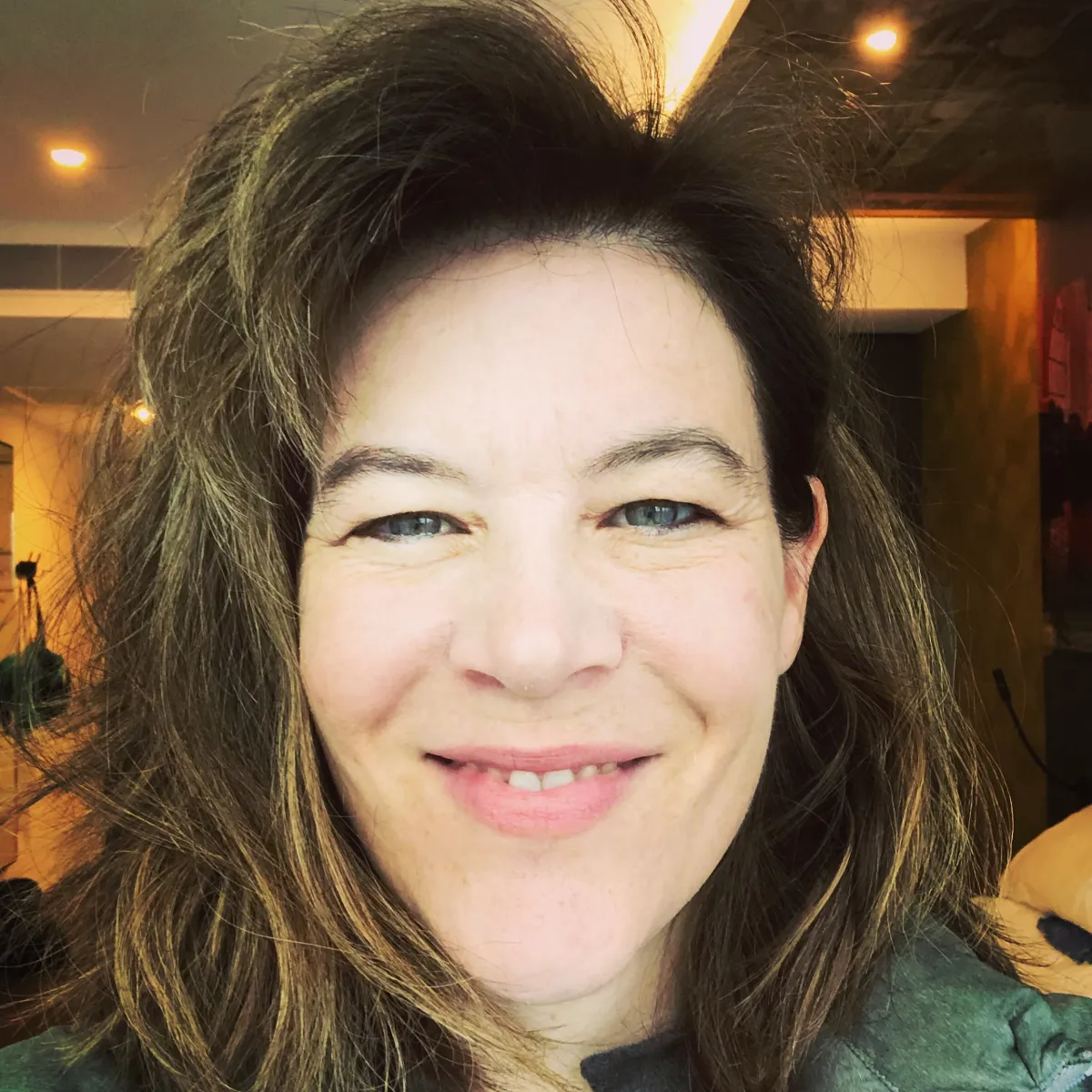 A white woman with shoulder length brown hair smiles broadly.