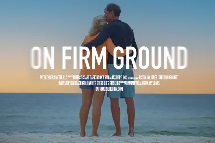 A couple faces the ocean in an embrace, the man holding his wife and kissing her head. The title "ON FIRM GROUND" over the image.