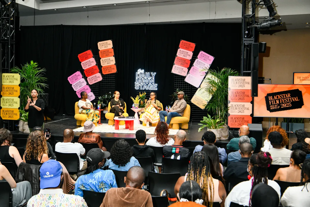 Four people sit on stage recording a podcast, in front of a live audience.