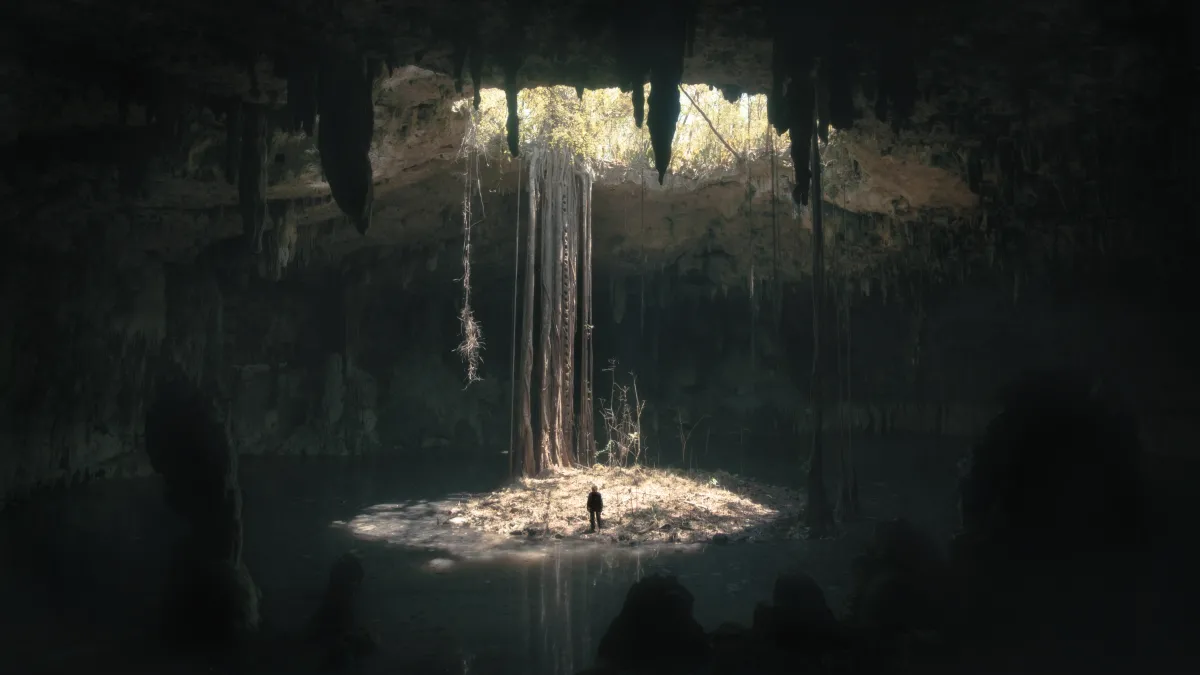From far away, a film still of a man standing in a shaft of light in a vast underground cavern.