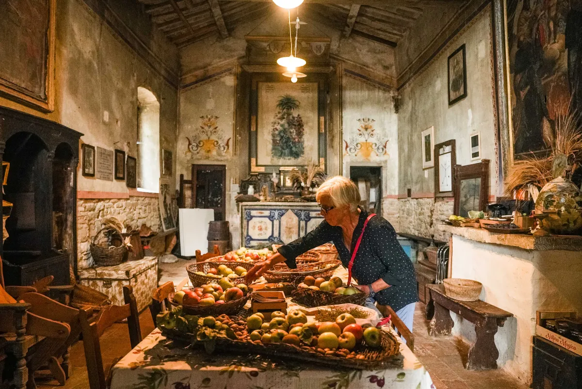 A 60-something-year-old woman examines baskets of apples on a table in a 14th Century church.