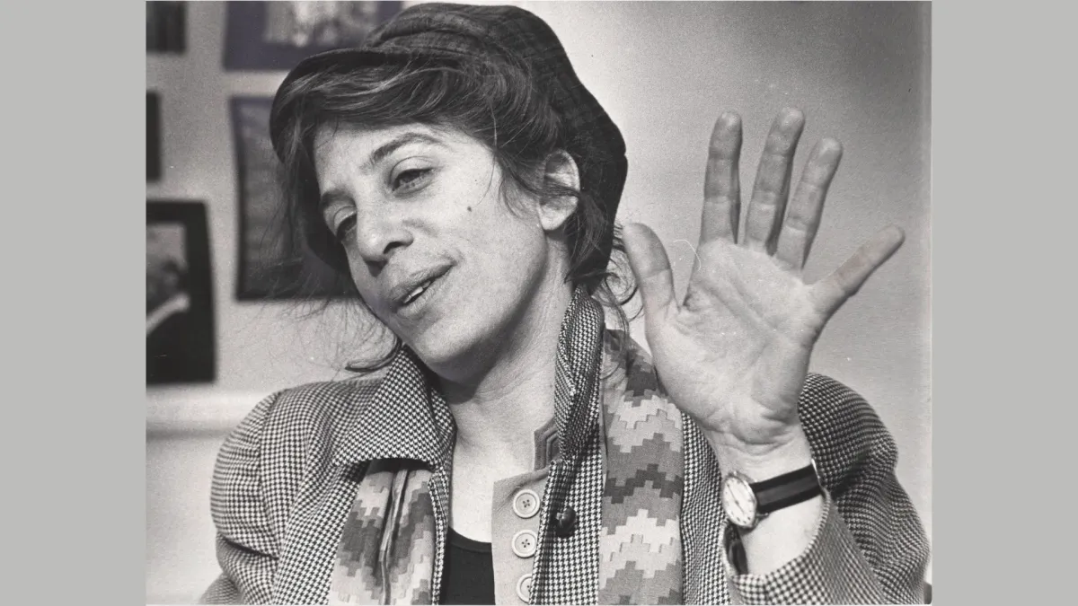 Black and white photo of a white woman with dark hair pulled back under a hat, wearing a scarf and a coat