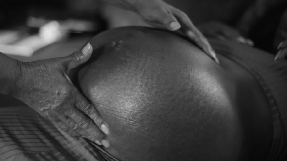 Black and white image of a pregnant woman's belly with the midwive's hand gently holding it.