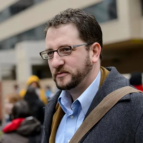 Headshot of Craig Aaron, a man with brown hair, glasses and a beard outside of the Federal Communications Commission
