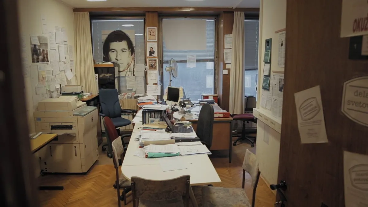 An empty, cramped office with plenty of strewn papers and posters covering every wall