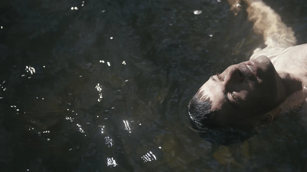 A white man with dark hair and hazel eyes looks up as he floats on a body of water