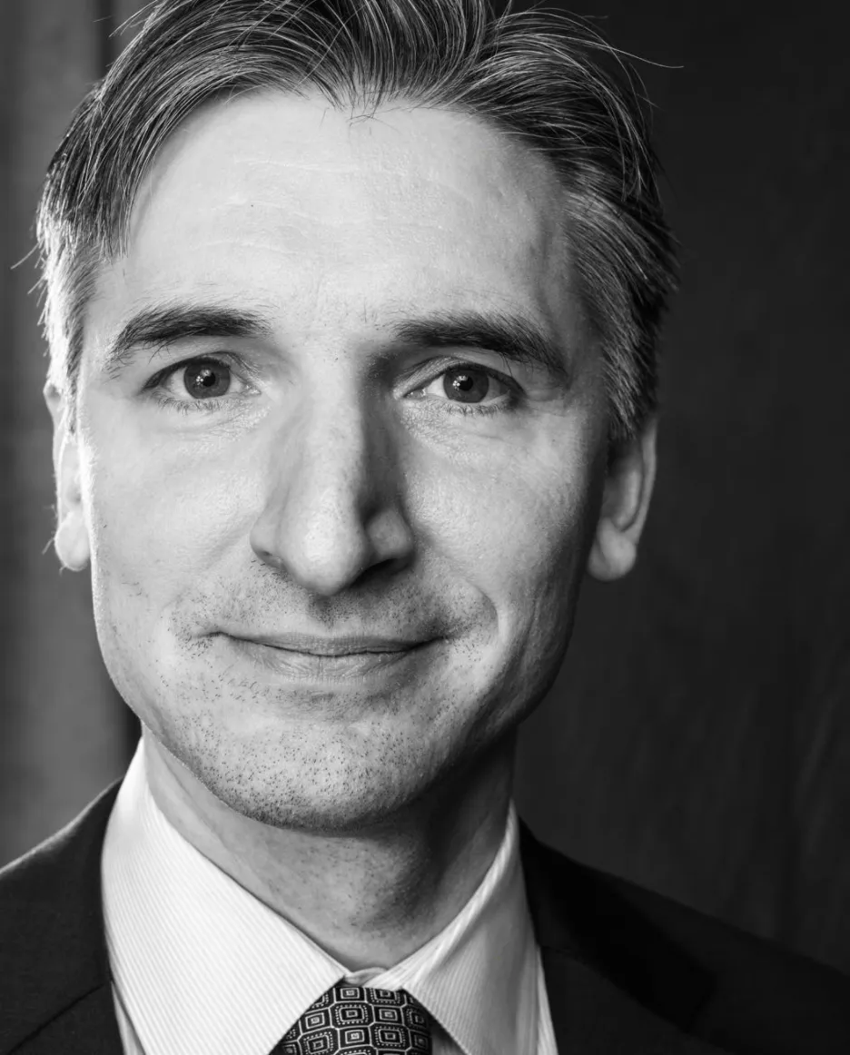 Black and white headshot of a middle-aged white man with short-cropped hair in a suit smiling at the camera