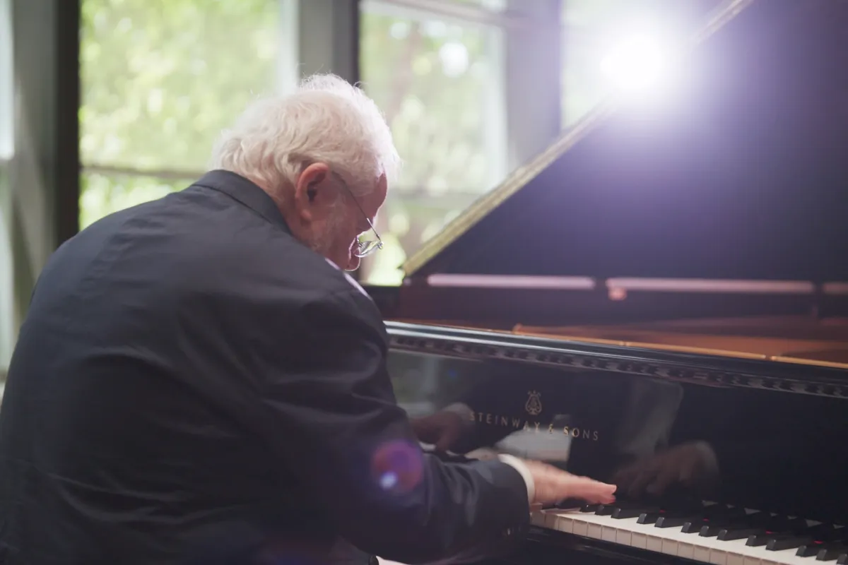 Over the shoulder shot of an older man wearing a suit jacket playing the piano