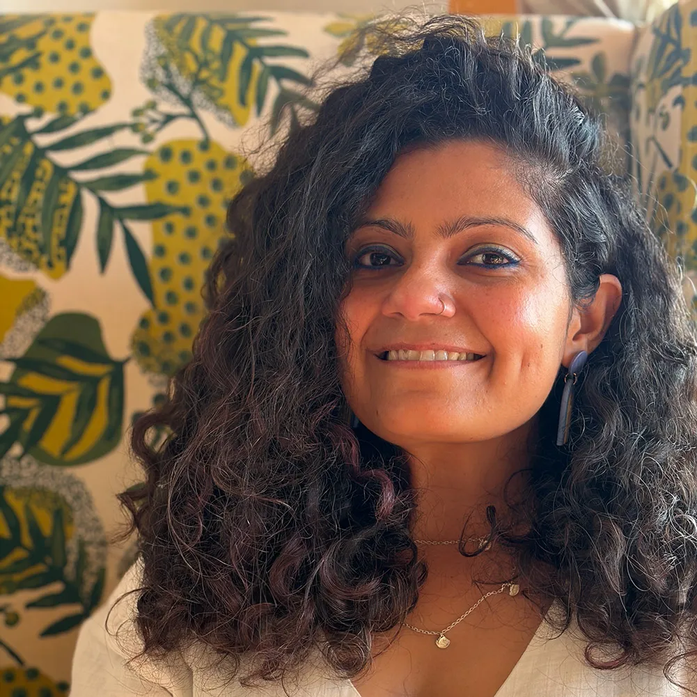 A brown woman with curly black hair smiles.